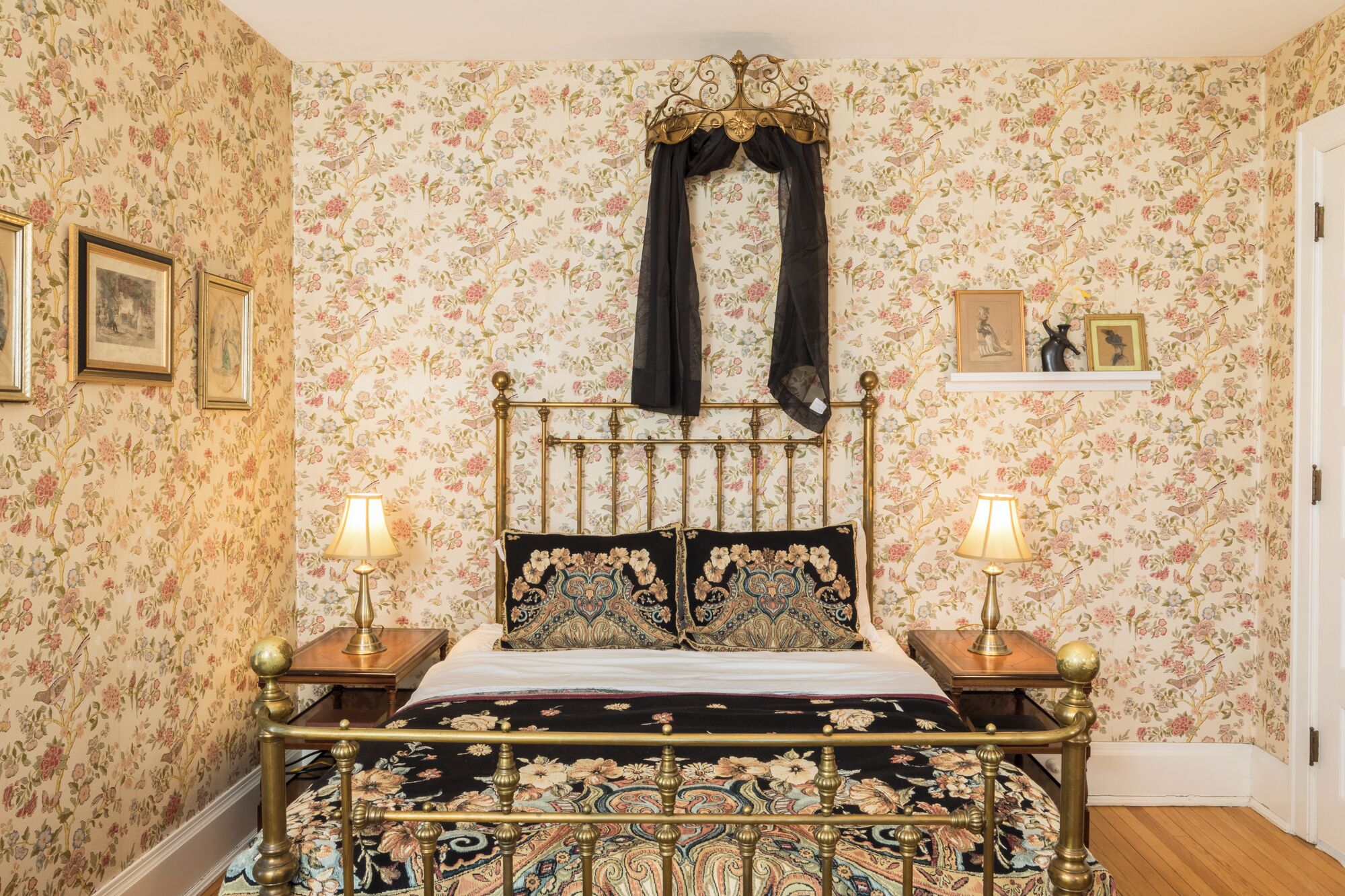A room with a bed, two bedside tables, a wall-mounted lamp, and floral wallpaper.