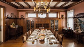 Uma sala de jantar com uma mesa de madeira comprida posta para uma refeição, rodeada por cadeiras.