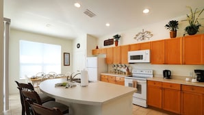 A kitchen with wooden cabinets, a white island with seating, a microwave, and a stove. - Single Level Luxury Villa with Pool and Hot tub close to Disney (Kissimmee)