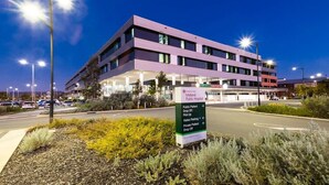A modern hospital building with a sign indicating public patient drop-off and visitor parking.