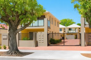 A residential building with a gated entrance, a tree in the foreground, and a clear sky. - Midland Apt, Hospital, Shops, Train, Sleeps 6 (Midland)