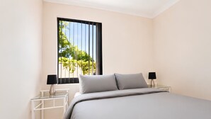 A bedroom with a bed, two bedside tables, and a window with a view of greenery.