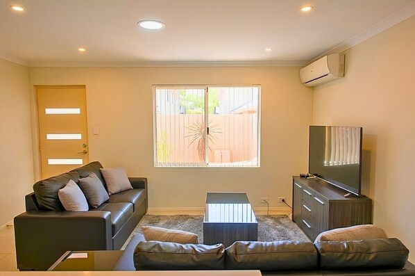 A living room with a sofa, a coffee table, a TV, and a window with blinds.