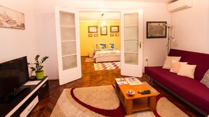 Quarto com televisão, planta, sofá vermelho e cama com parede amarela e quadros.