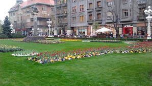 Uma praça pública com um jardim de flores e edifícios ao fundo.