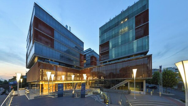 Um edifício moderno com fachada de vidro e base de tijolos, apresentando um átrio central com escadaria e rampa.