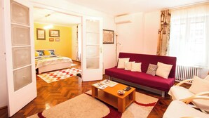 Uma sala de estar aconchegante com um sofá vermelho, uma mesa de centro de madeira e uma cama com um edredom colorido.