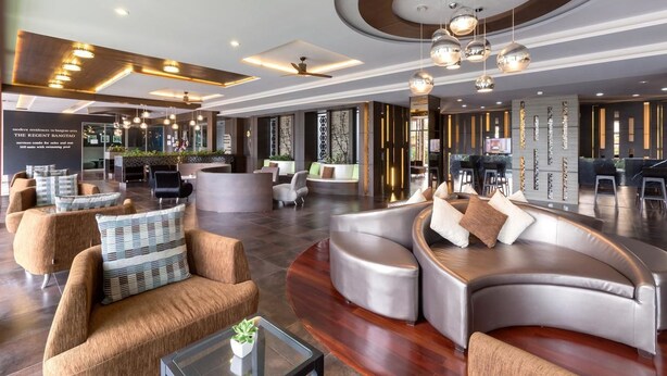 Un hall d’entrée spacieux, doté d’un mobilier moderne, notamment des canapés et des fauteuils en cuir, un comptoir de réception, et un plafond agrémenté d’un éclairage encastré et d’un lustre central.