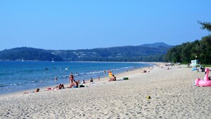Une plage où l’on peut voir des gens se prélasser au soleil et nager, une tour de surveillance des sauveteurs et un ciel dégagé.