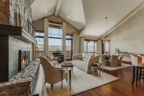 A spacious living room with a stone fireplace, large windows, and a high ceiling.