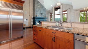 A modern kitchen with a stainless steel refrigerator, wooden cabinets, granite countertop, and a stone fireplace.