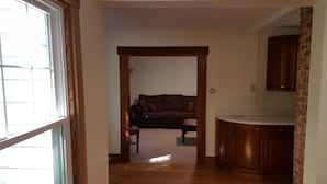 A hallway leading to a living room with a couch and a kitchen area with wooden cabinets. - Manchester Walking distance to all shops and restaurants quick ride/lakes |hikes (manchester center)