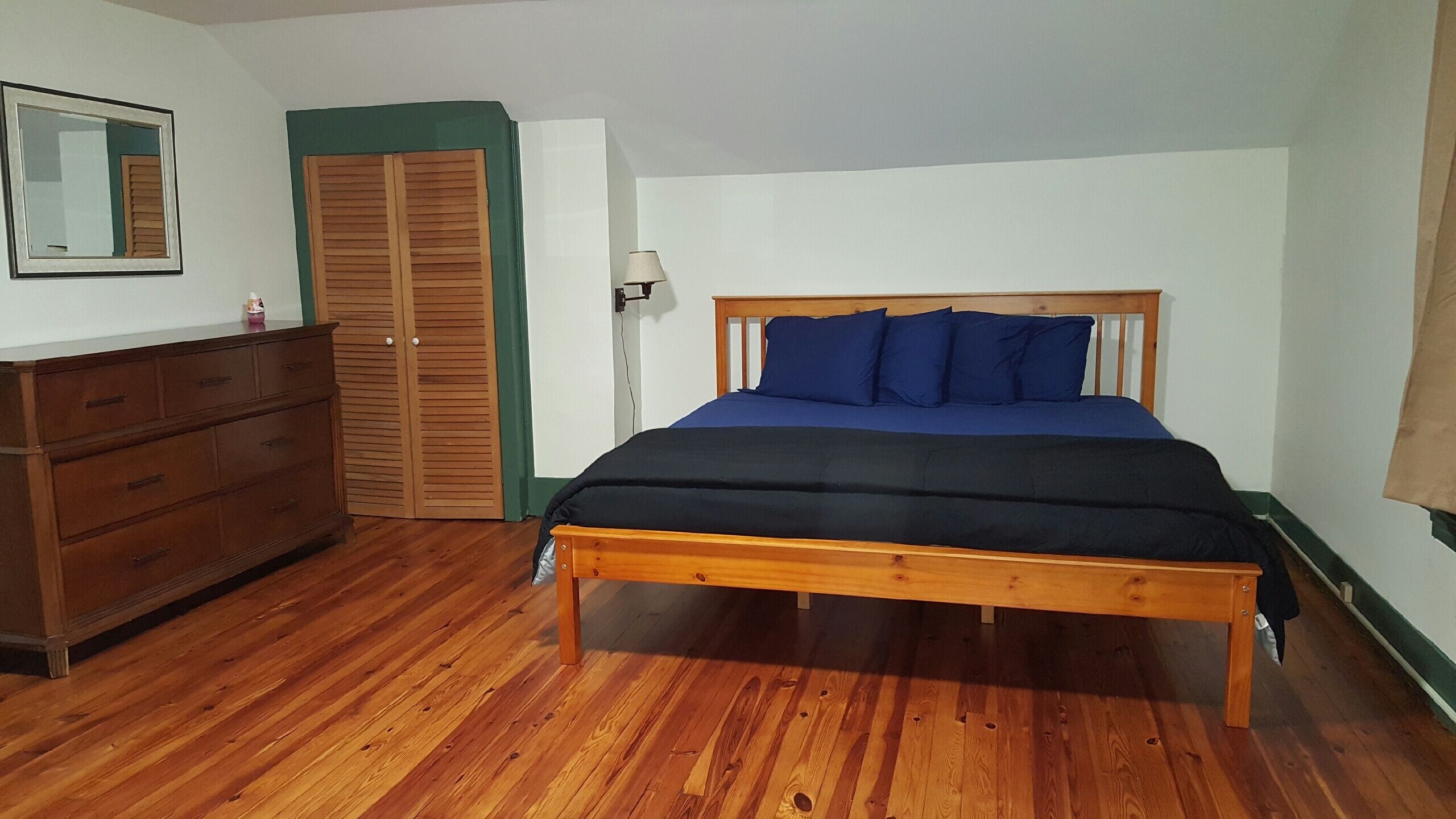 Een slaapkamer met een houten bed, een dressoir, een kledingkast en een spiegel.