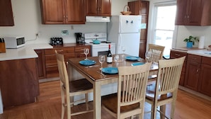 A kitchen with wooden cabinets, a dining table set for four, and a refrigerator. - Manchester Walking distance to all shops and restaurants quick ride/lakes |hikes (manchester center)