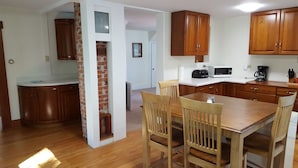 A kitchen with wooden cabinets, a dining table with chairs, and a microwave. - Manchester Walking distance to all shops and restaurants quick ride/lakes |hikes (manchester center)