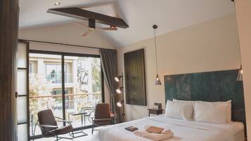 A modern hotel room with a large bed, a balcony with a table and chairs, a ceiling fan, and a view of the outside.