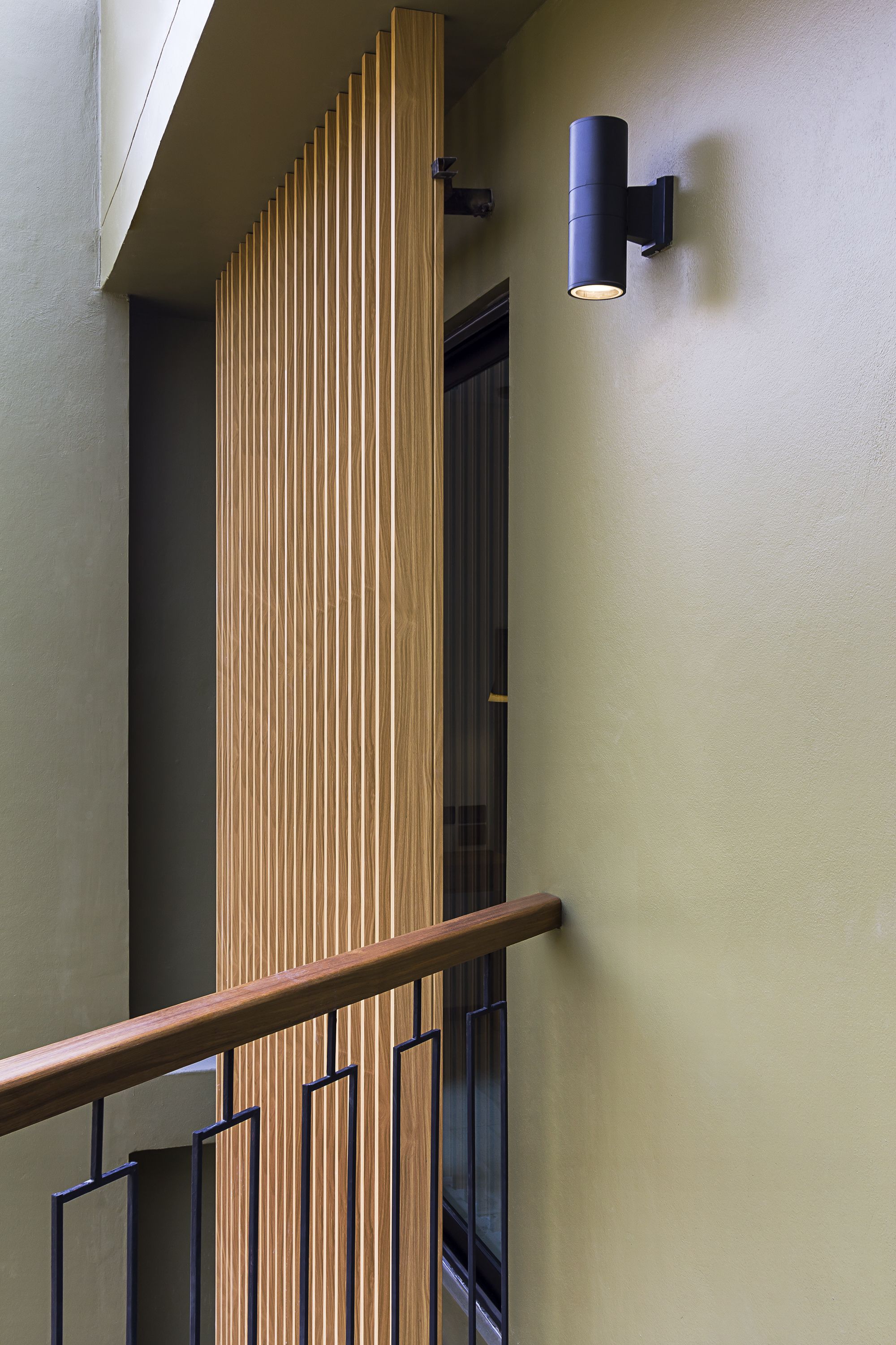A modern interior with a wooden slatted wall, a black wall-mounted light fixture, and a metal railing.