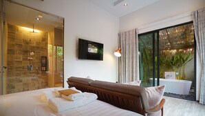 Une chambre d’hôtel moderne dotée d’un grand lit, d’une douche à parois de verre, d’une baignoire et offrant une vue sur la verdure environnante.