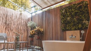 Une salle de bain extérieure moderne avec un mur en bois, un paravent en bambou et un grand bac à plantes orné de feuillage verdoyant.