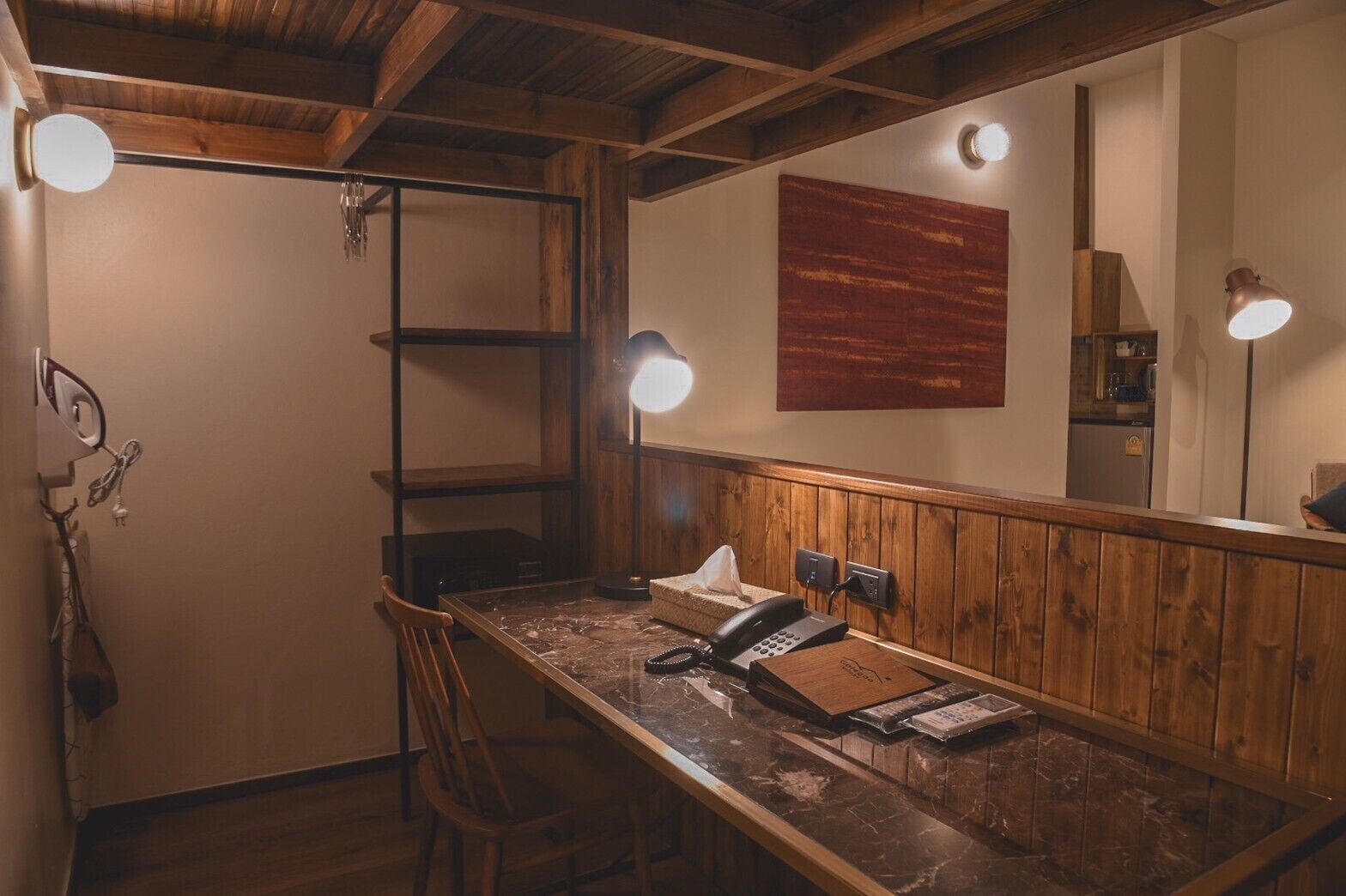 A wooden-framed room with a desk, chair, and a telephone. There are three wall-mounted lights and a large mirror.