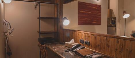 A wooden-framed room with a desk, chair, and a telephone. There are three wall-mounted lights and a large mirror.
