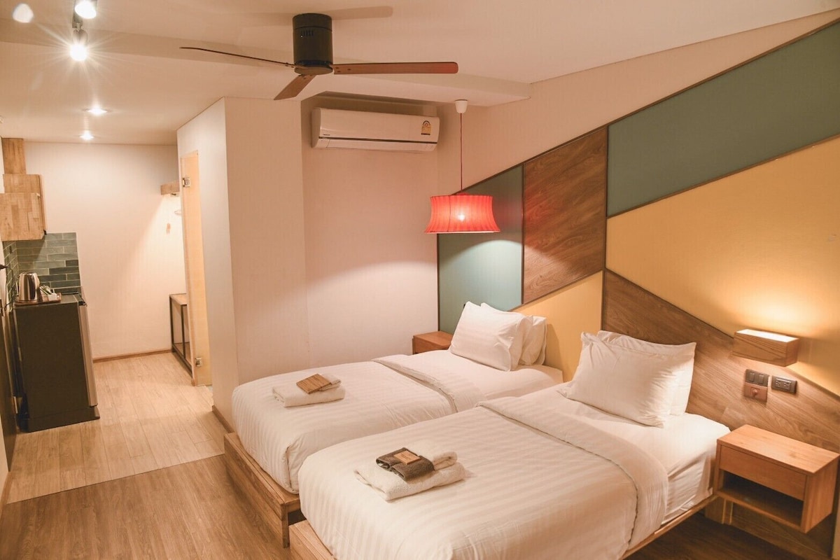 A hotel room with two beds, a ceiling fan, a red lamp, and a wooden nightstand.