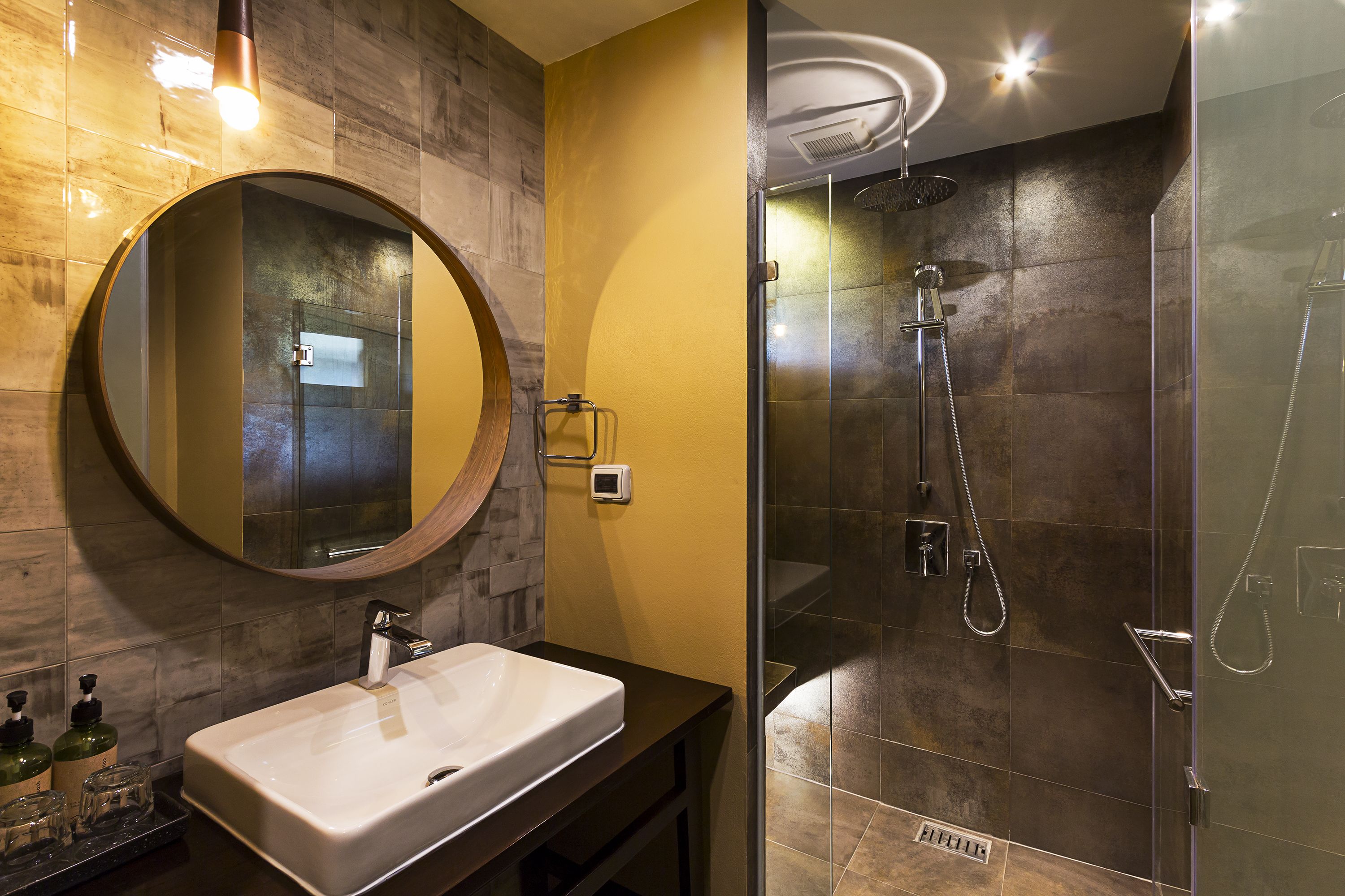 Un baño con un espejo redondo, un lavabo blanco y una zona de ducha con mampara de vidrio.
