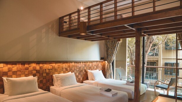 Une chambre d’hôtel avec deux lits, une tête de lit en bois et un balcon avec des chaises.