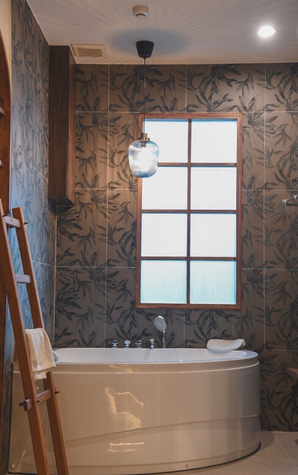 Een badkamer met een groot bad, een raam met zonwering en een hanglamp.