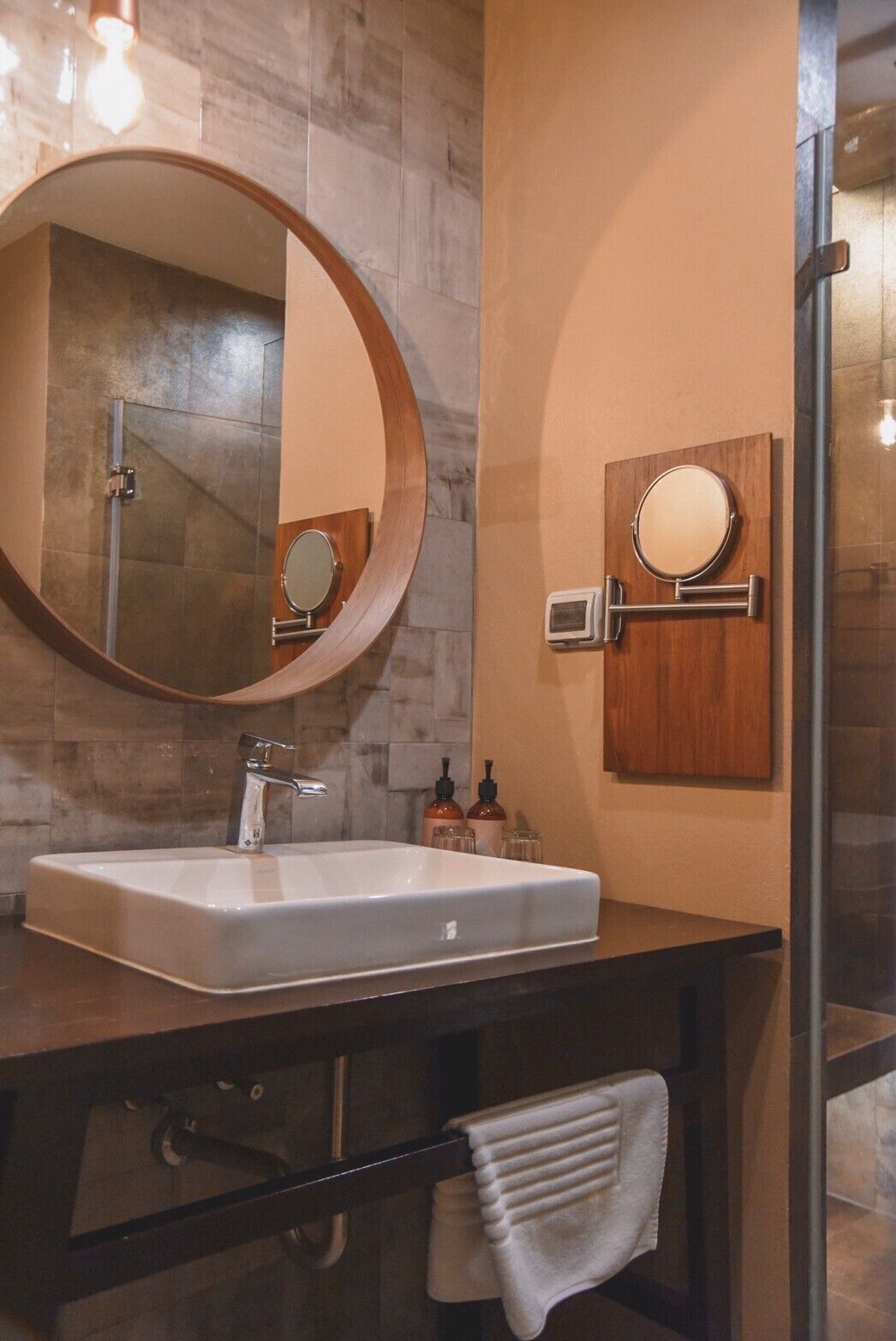 A bathroom with a rectangular sink, a round mirror, and a towel rack.