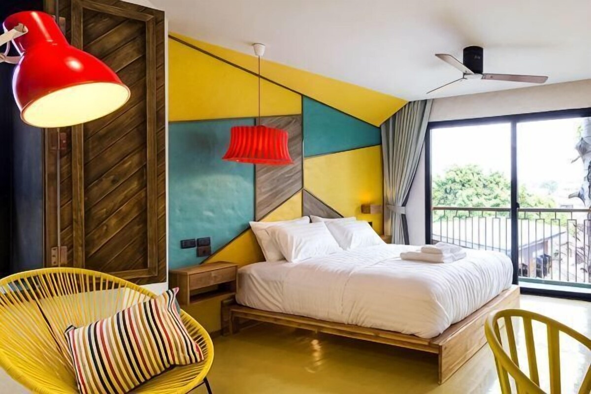 A bedroom with a bed, two chairs, a red lamp, and a ceiling fan.