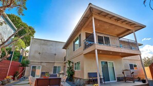 Une maison à deux étages dotée d’un balcon, d’un espace extérieur aménagé pour s’asseoir et d’une terrasse.