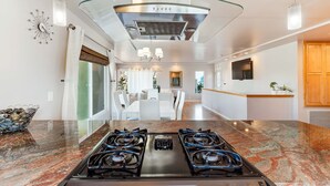Une cuisine moderne dotée d’une cuisinière à gaz, d’un plafond en verre et d’un coin repas avec des meubles blancs.