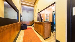 Un vestíbulo de hotel con un mostrador de recepción de madera, una alfombra roja y un cuadro en la pared.
