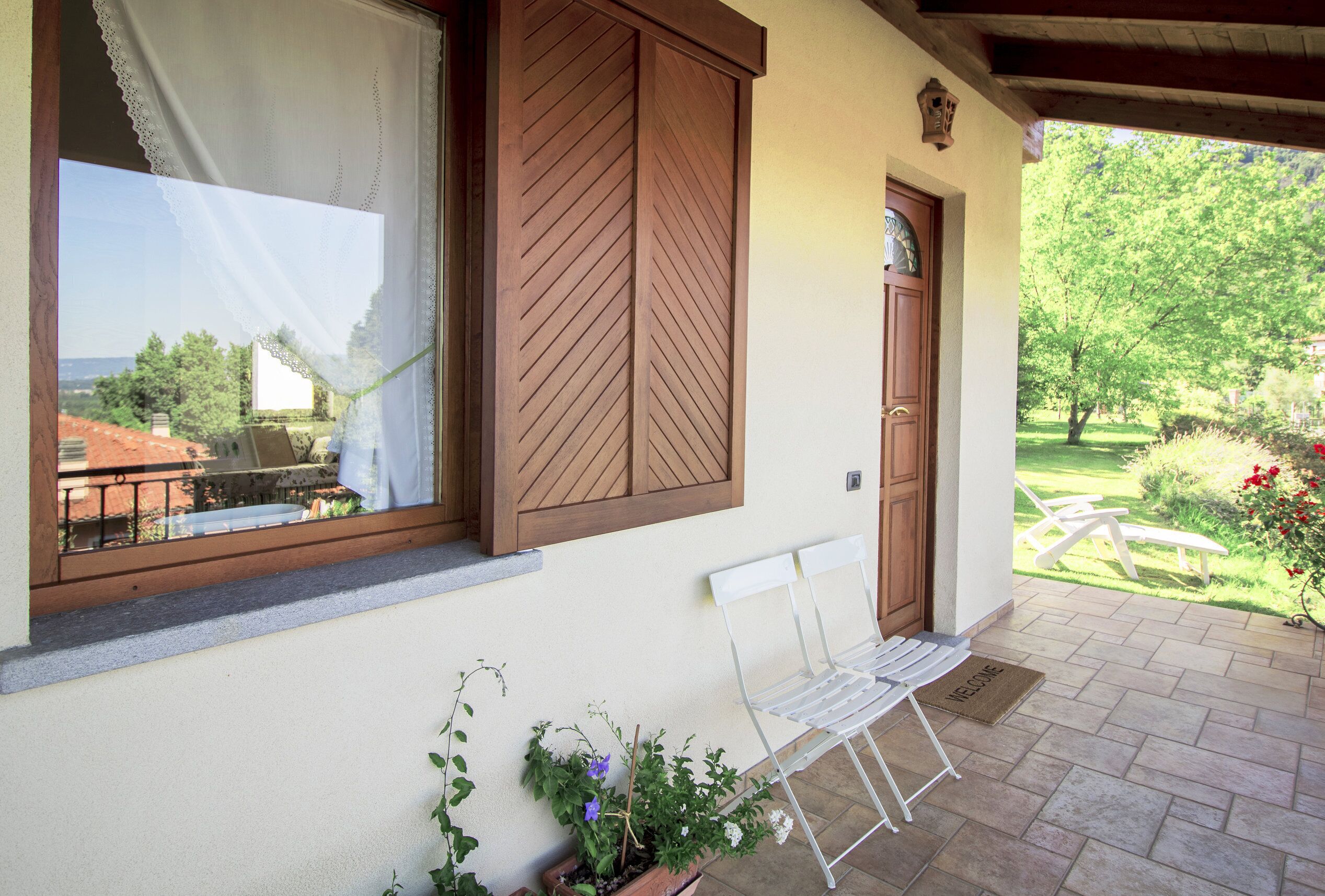 Eine überdachte Terrasse mit einem weißen Stuhl, einer Holztür und einem Fenster mit Rollläden.