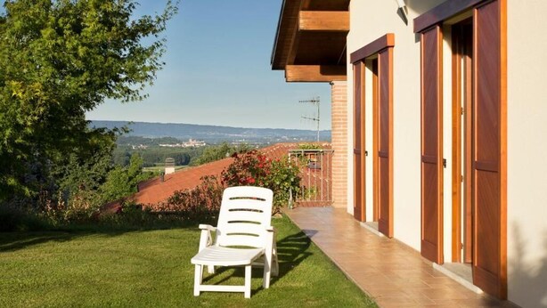 A patio with a white chair, a view of the countryside, and a building with wooden doors.
