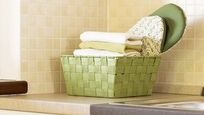 A kitchen with a green woven basket containing folded towels and a green cloth on a countertop.