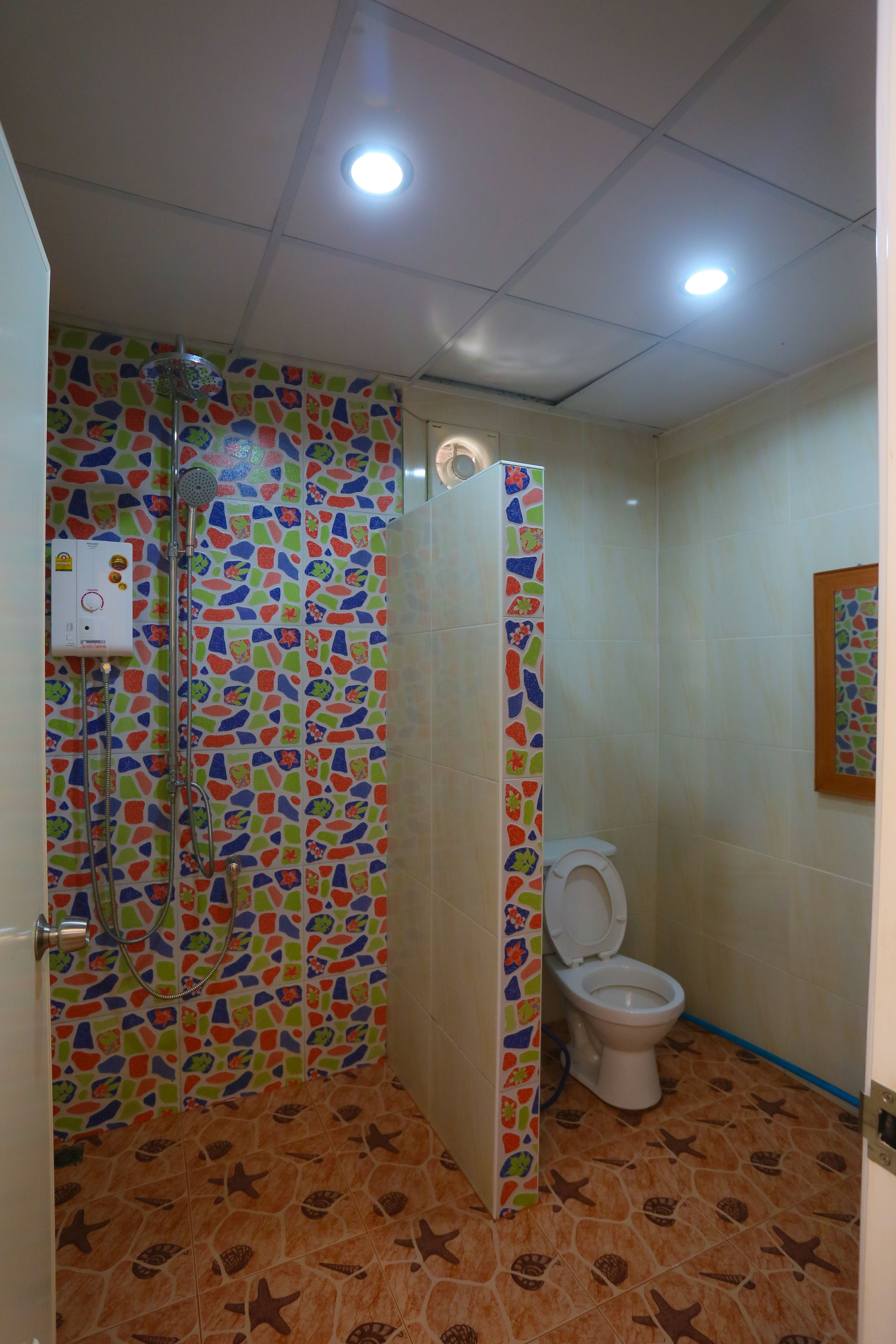 Un baño con ducha, inodoro y pared decorada con un mosaico de colores.