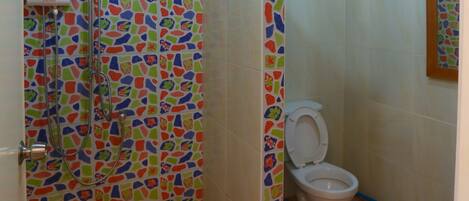 Un baño con ducha, inodoro y pared decorada con un mosaico de colores.
