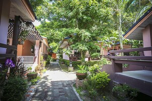 Un sendero bordeado por plantas en macetas y arquitectura tradicional, que conduce a una zona cubierta con vistas al follaje circundante.