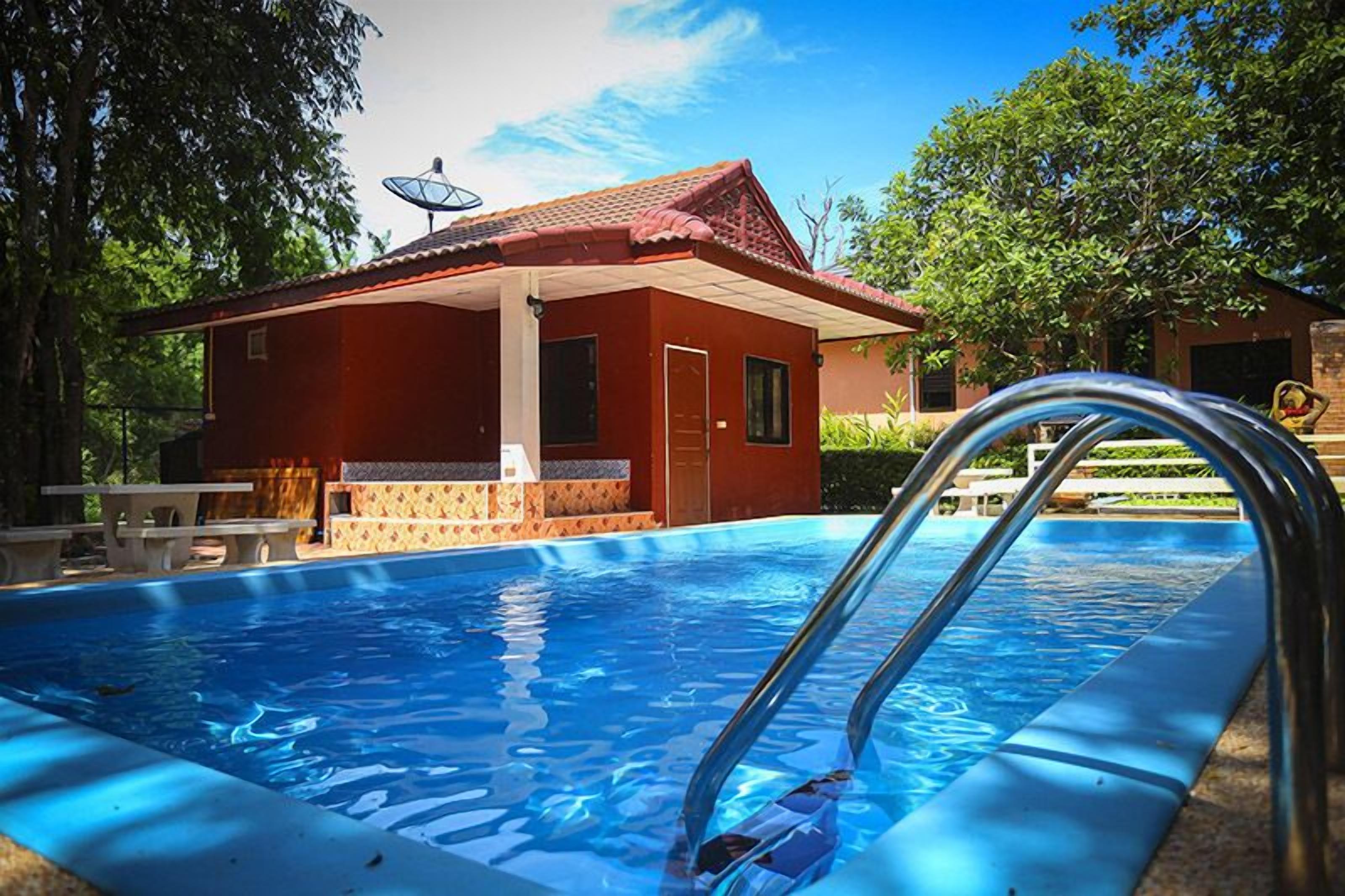 A swimming pool with a metal ladder, a red building with a tiled roof, and a satellite dish.
