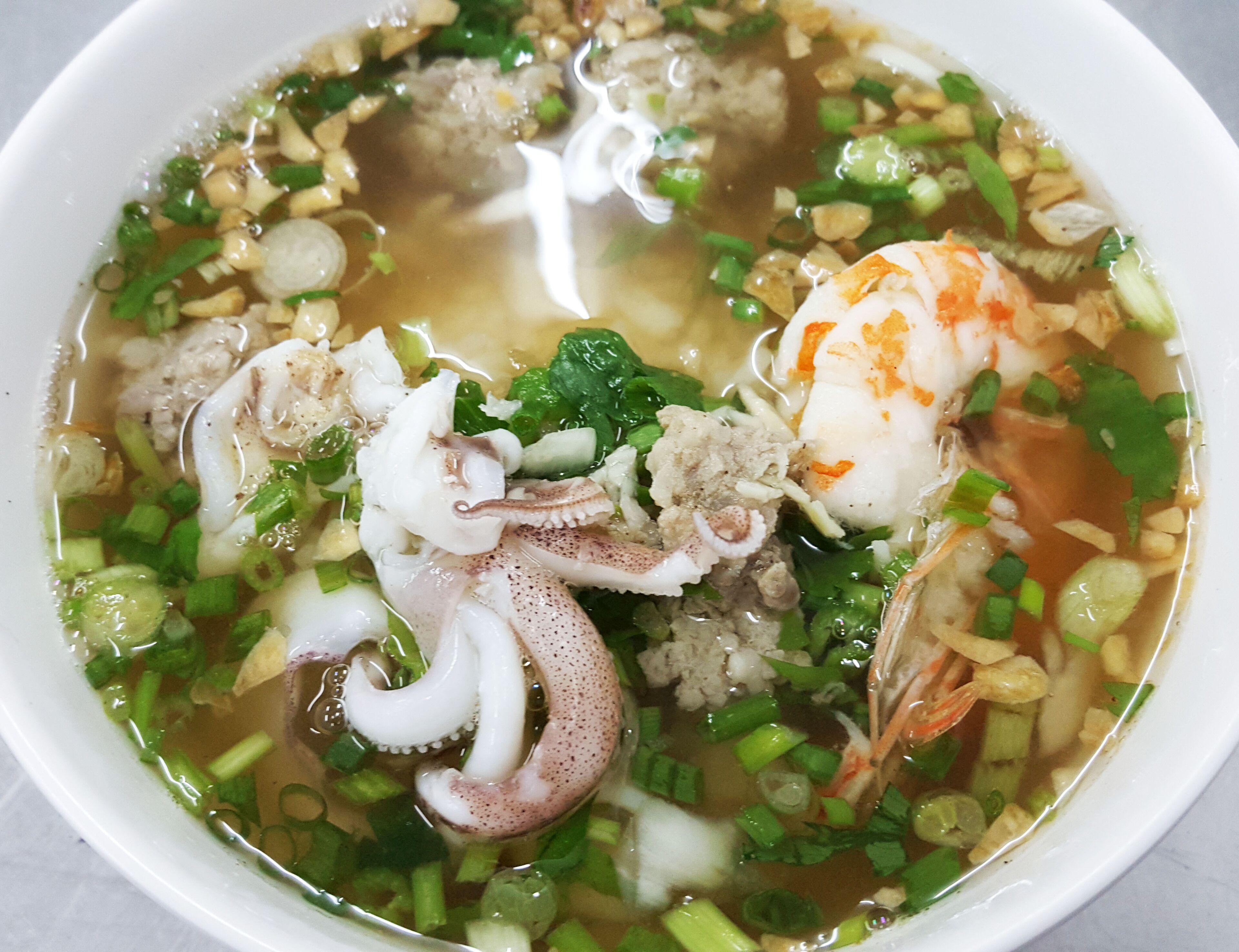 Un tazón de sopa de mariscos con diversos ingredientes, como camarones, calamares y cebollines.