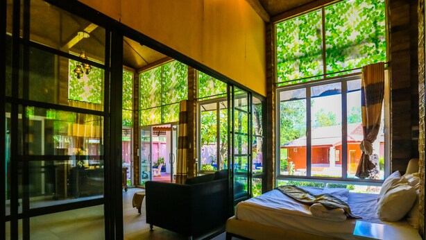 Ein Zimmer mit einem Bett, einem schwarzen Sofa und einem Fenster mit Blick auf Grünflächen und ein Gebäude.