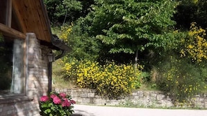A stone building with a brick chimney, a flower bed with pink flowers, and yellow flowers in the background.