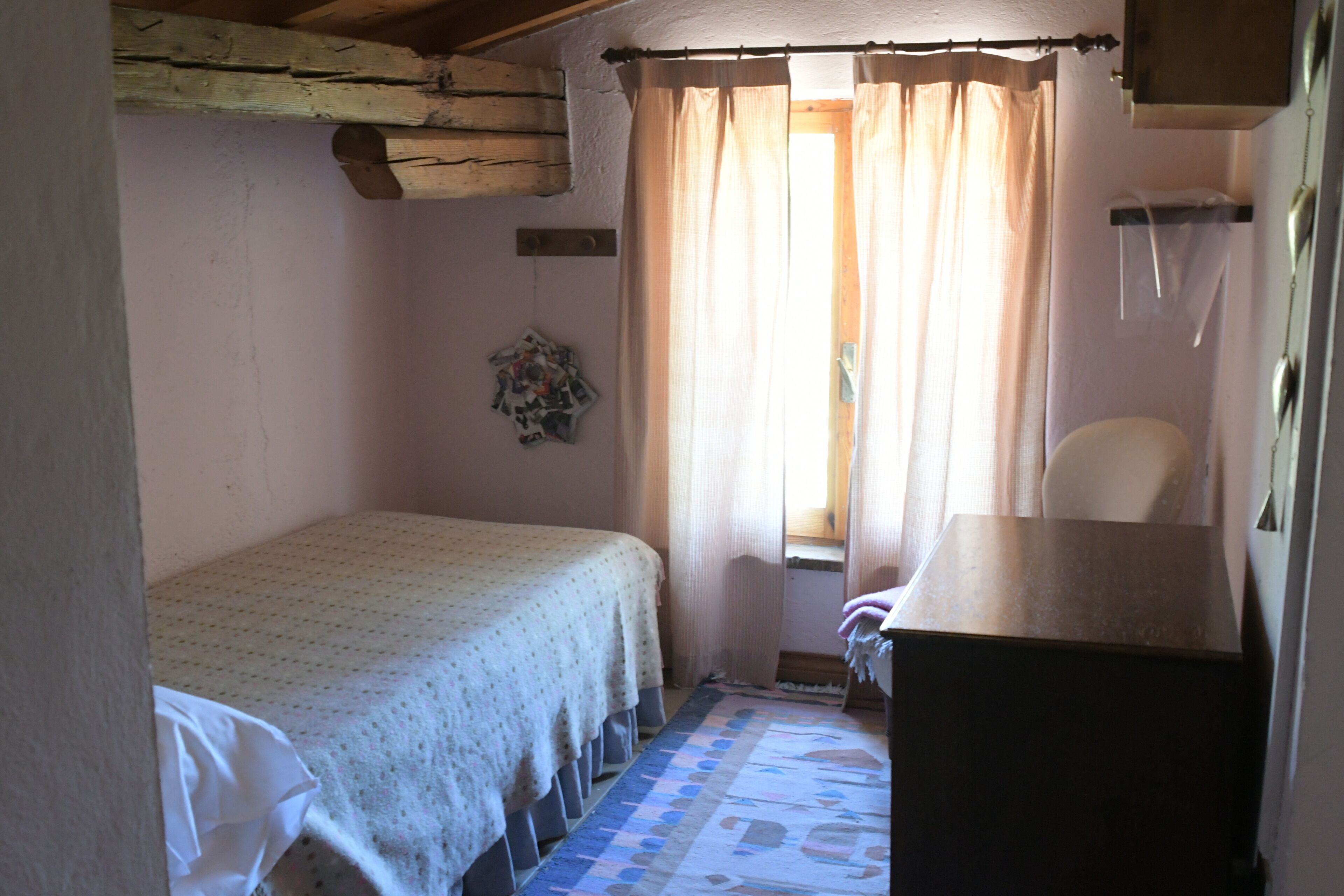 A small, cozy bedroom with a single bed, a wooden dresser, and a window with curtains.