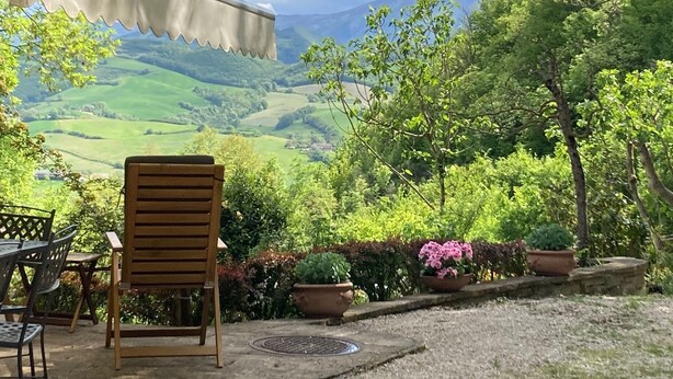 A wooden chair facing a scenic view of rolling hills and a mountain range under a clear sky.
