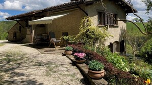 A rustic stone house with a tiled roof, a covered porch, and a gravel driveway.