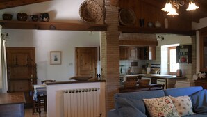 A cozy living room with a blue sofa, a dining area with a table, and a kitchen with wooden cabinets and a brick wall.