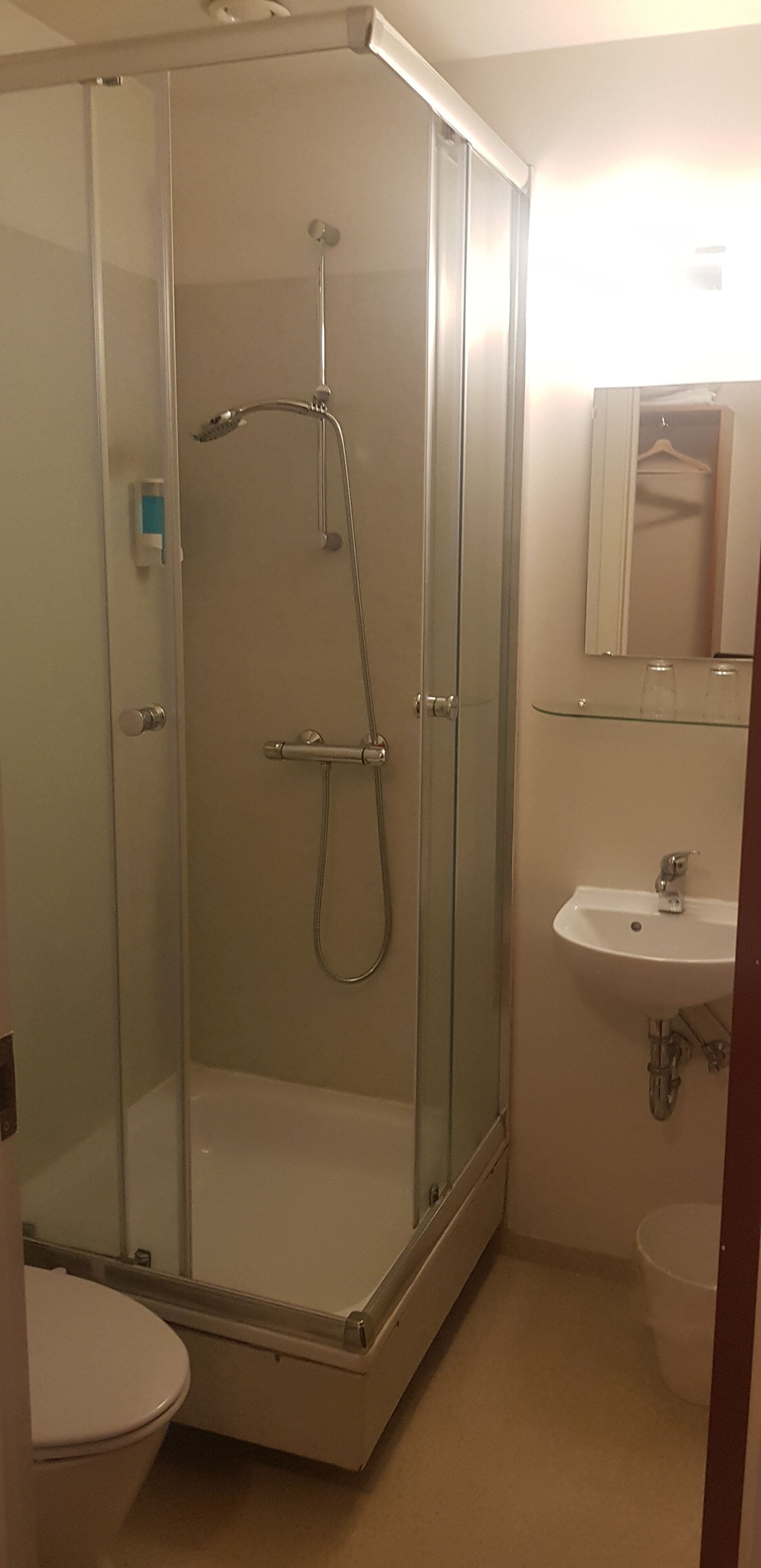 A glass-enclosed shower stall with a handheld showerhead and a wall-mounted faucet.