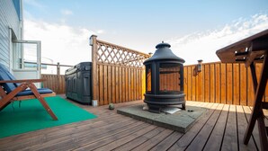Una terraza de madera con una chimenea de piedra, una parrilla y una silla de descanso.